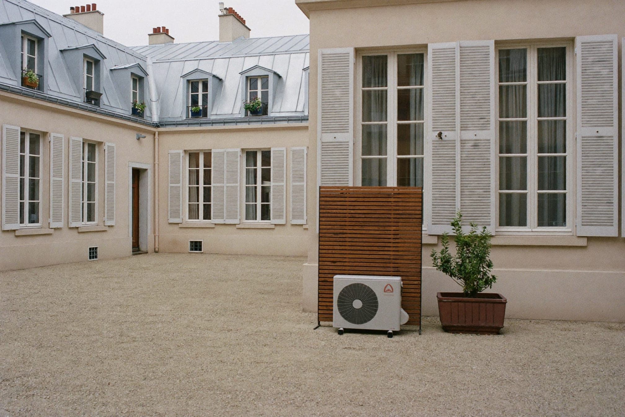 Cour intérieure parisienne avec une unité extérieure compacte derrière un écran acoustique, illustration générique