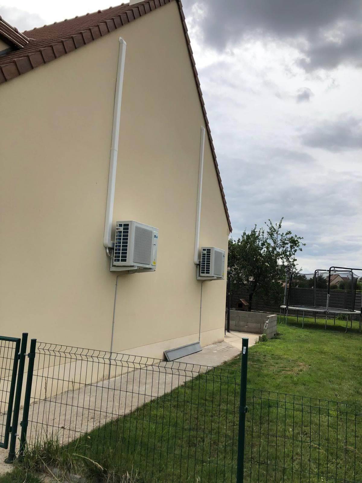 Deux unités extérieures de pompe à chaleur air/air fixées en pignon d’une maison, jardin au premier plan